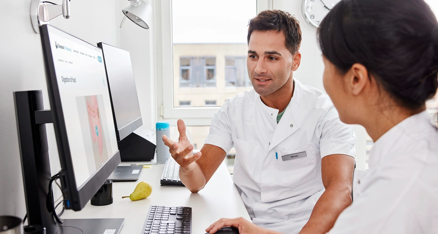 Foto van twee zorgverleners die achter een computer zitten. Multiple Sclerose kan darmproblemen veroorzaken. Er zijn verschillende behandelopties om de symptomen te behandelen en te beheersen. 