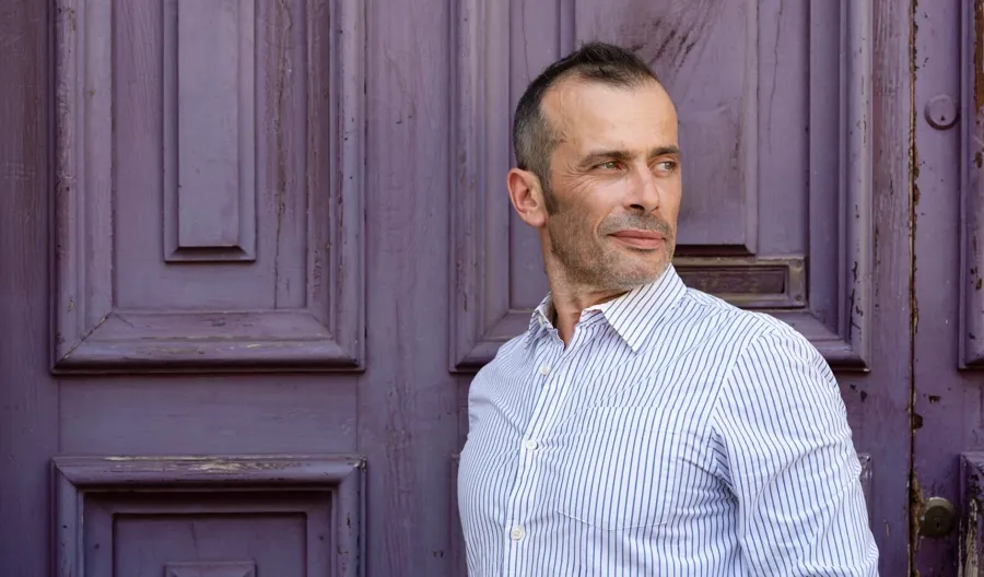 Portretfoto van Andrea voor een paarse deur. Andrea kreeg de diagnose Progressieve Relapsing Multiple Sclerose en kreeg problemen met zowel zijn blaas als zijn darmen. 