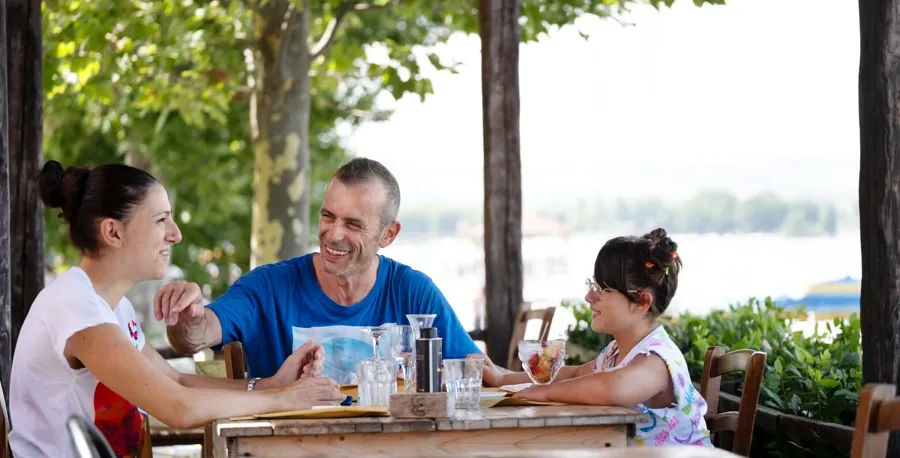 Andrea zit samen met zijn familie aan een tafel in een restaurant. Als je vragen of zorgen hebt over je blaas en darmen wanneer je MS hebtt, neem dan contact op met Coloplast Care voor ondersteuning. 