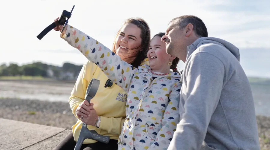 Foto van Sarah en haar gezin die samen een selfie maken op het strand. Het heeft lang geduurd voordat Sarah haar blaasklachten in verband bracht met haar MS-diagnose. 