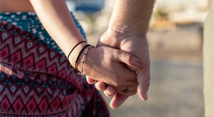Closeup image of couple holding hands. Other MS symptoms like fatigue, tremor, or bladder and bowel issues may interfere with an individual’s sex life. 